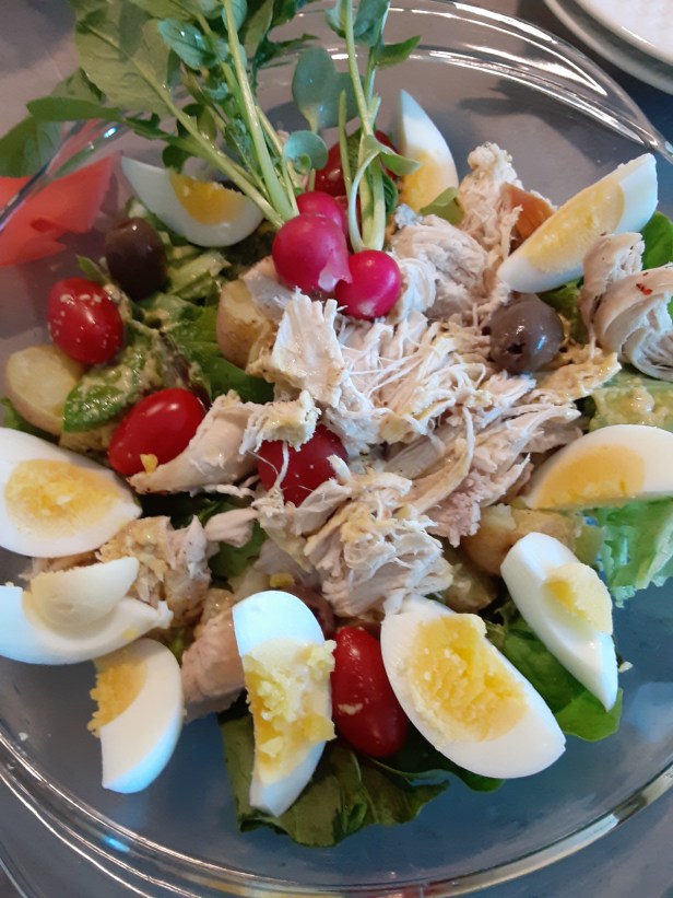 chicken and eggs on fresh greens, radishes, olives and potatoes